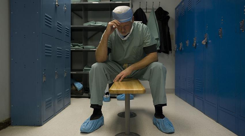 A doctor in scrubs rests in a locker room
