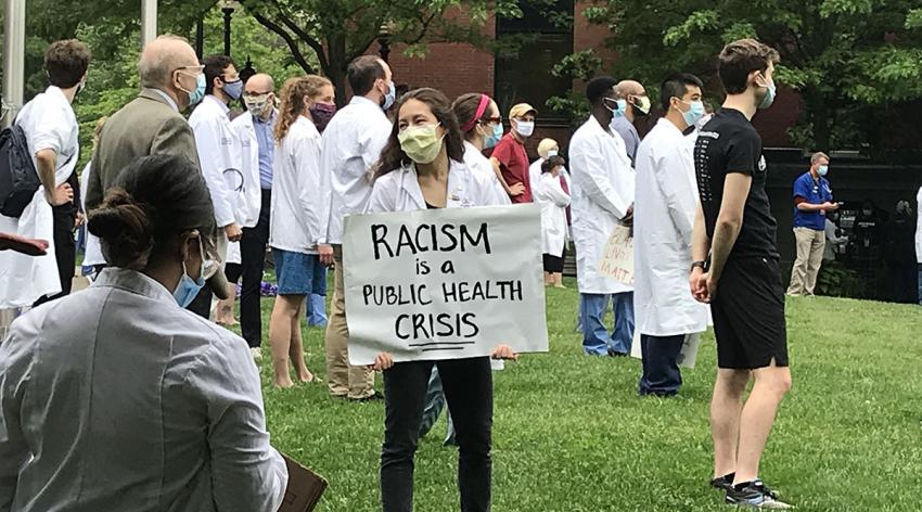 A student holds a sign that says "Racism is a public health crisis"