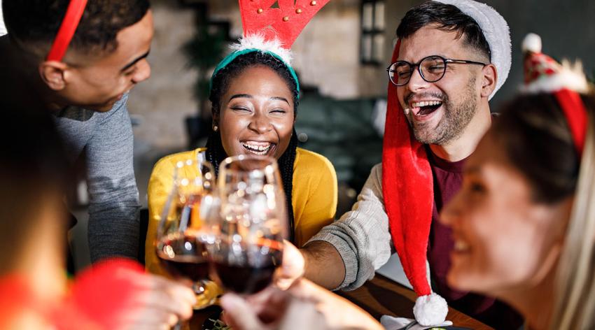 A group of diverse adults dressed in holiday attire toast each other holding glasses 