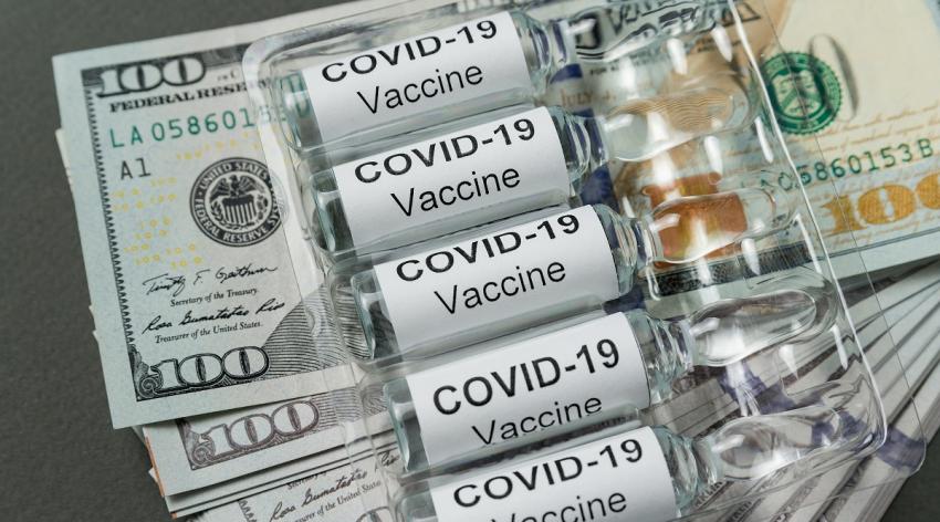US dollars with COVID-19 vaccine vials on top