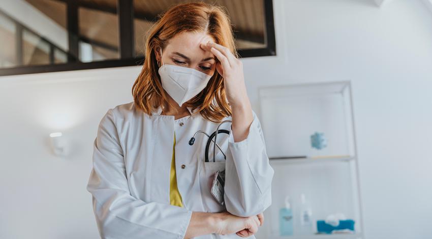 Doctor wearing protective face mask standing with head in hands at clinic