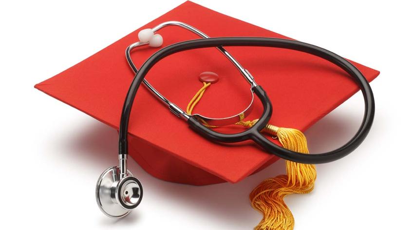 Stock image of a stethoscope on top of a red graduation cap against a white background. 