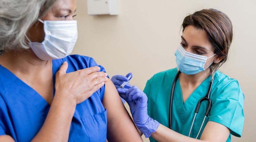 A medical professional in scrubs gives the COVID-19 vaccine to another medical professional
