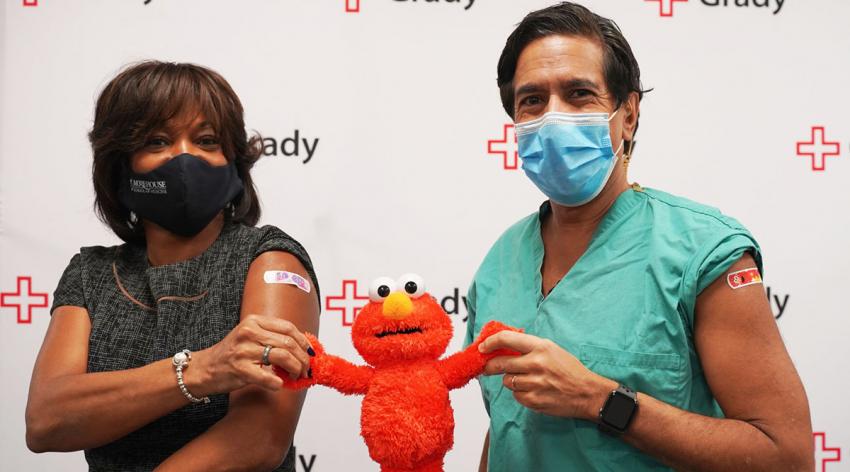 Valerie Montgomery Rice, MD, president and dean of Morehead School of Medicine, and medical correspondent Sanjay Gupta, MD, celebrate their COVID-19 inoculations with Elmo, who has been deployed to help answer children’s questions about the vaccines.