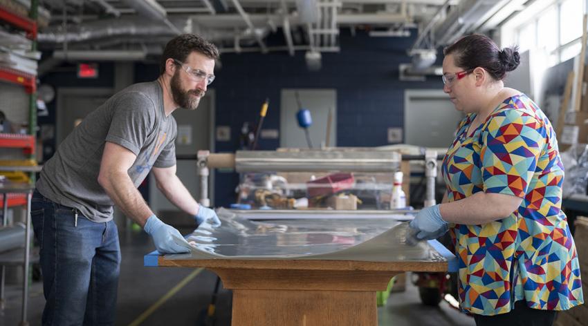 Trevor Kemp, assistant manager of the University of Virginia School of Architecture’s FabLab, and Melissa Goldman, manager of the FabLab, prepare plastic film to be cut for face shields