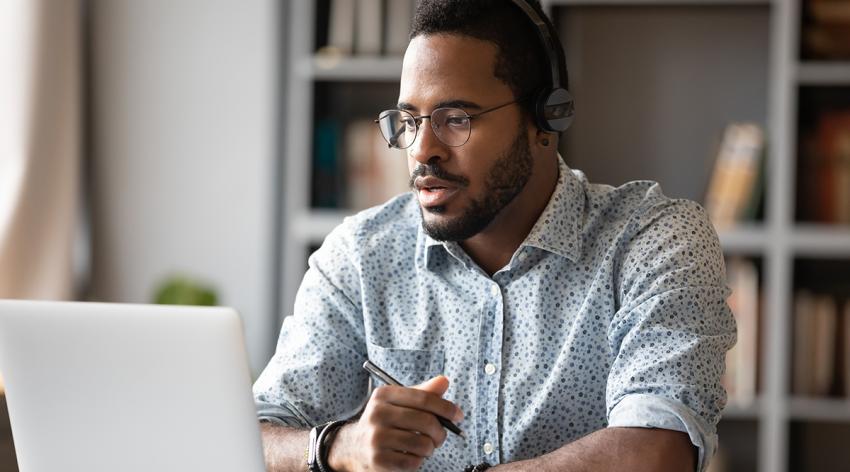 Focused young African businessman wearing headphones, studying online