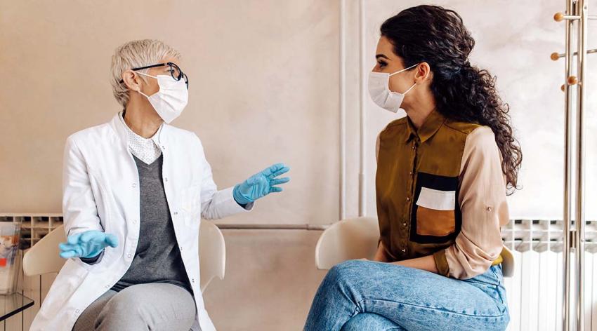 Female medical professional speaking with a woman, each wearing masks