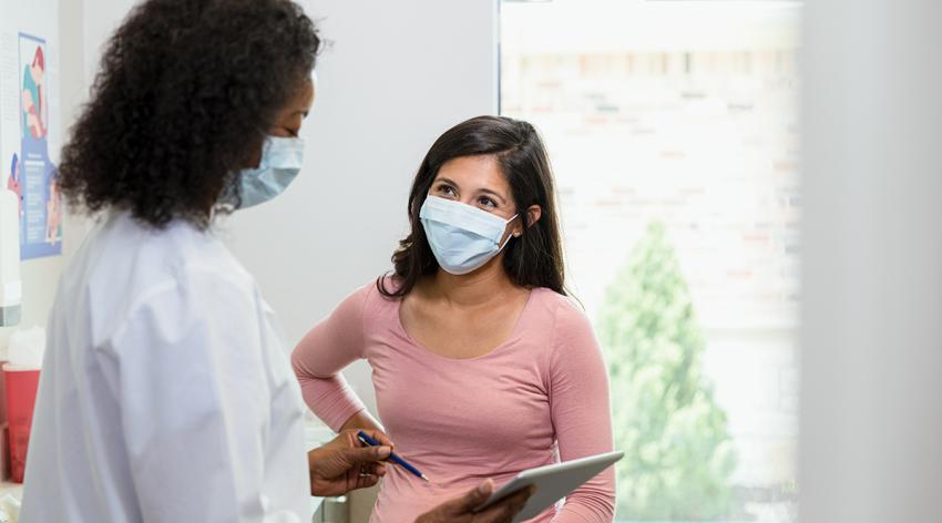 A mature adult doctor and her patient both wear masks to the consultation to slow the spread of illness.