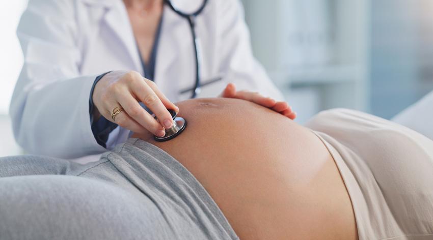 A female doctor using a stethoscope on a pregnant woman's stomach