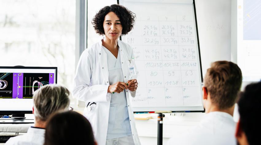 A female medical faculty standing in front of her students inside a classroom. Behind 