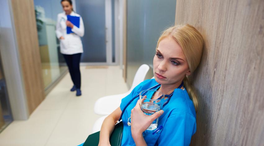 Surgeon sitting in hospital hallway, holding glass of water, pensive expression