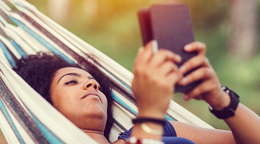 Young girl reading e-book in a hammock