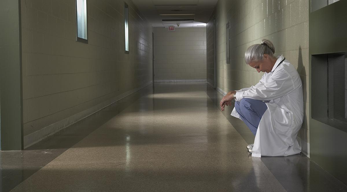 A woman in scrubs kneeling in a hallway.