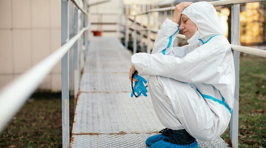 A provider in a full protective suit takes a break outside while looking stressed